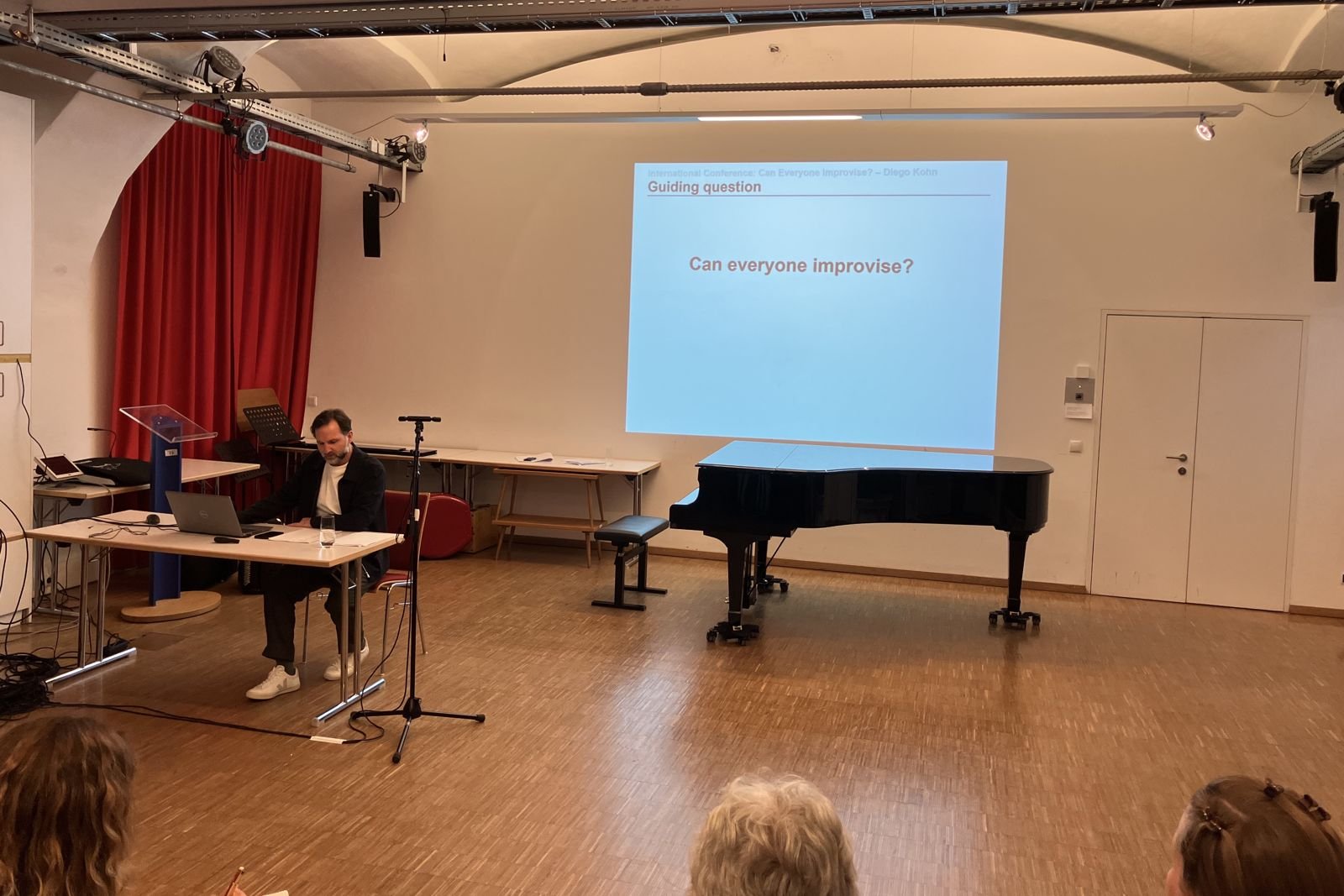 The lecture room at KUG Graz with a grand piano and the projected question: Can everyone improvise?